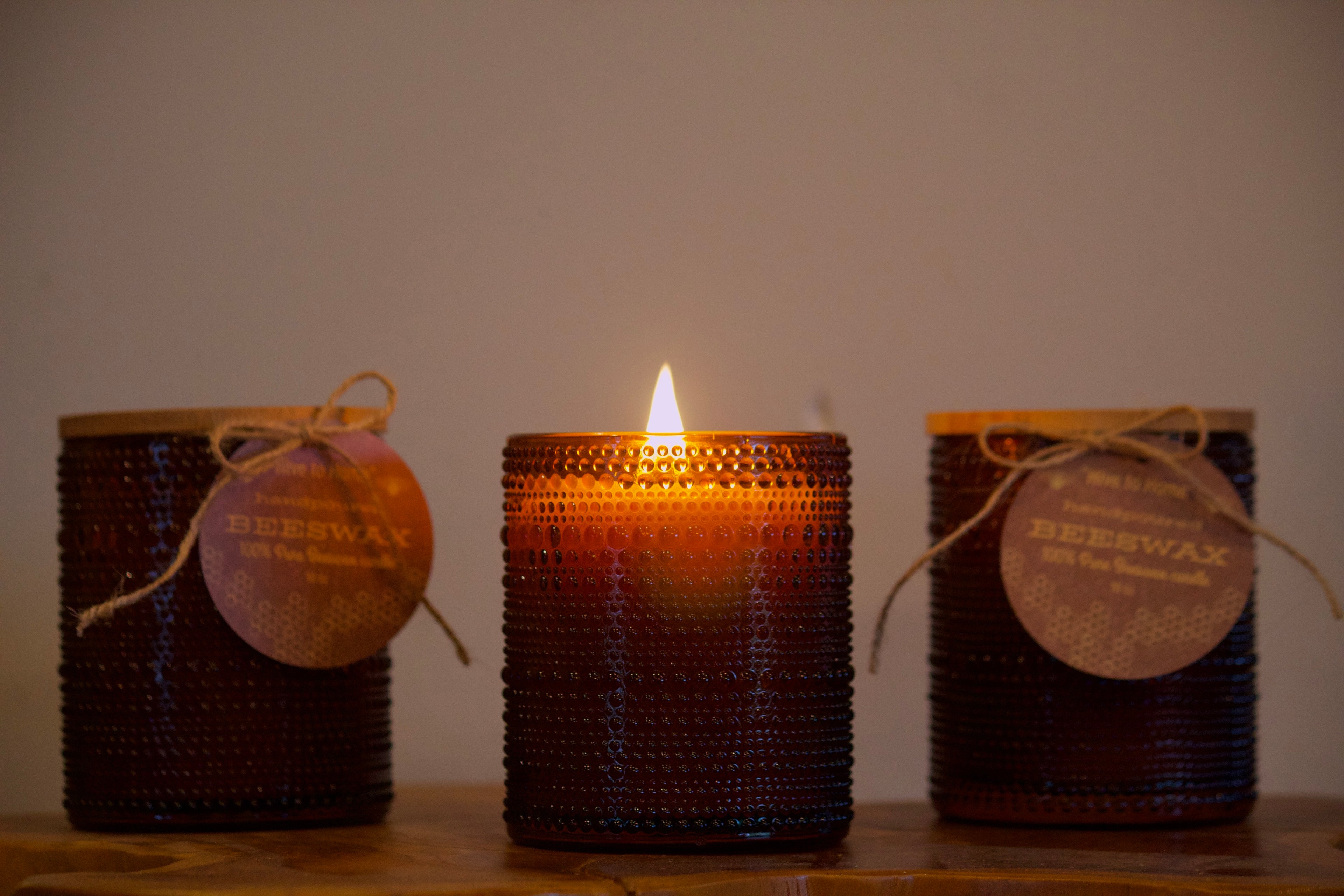Three beehive-patterned beeswax candles with wooden lids on a wooden surface.