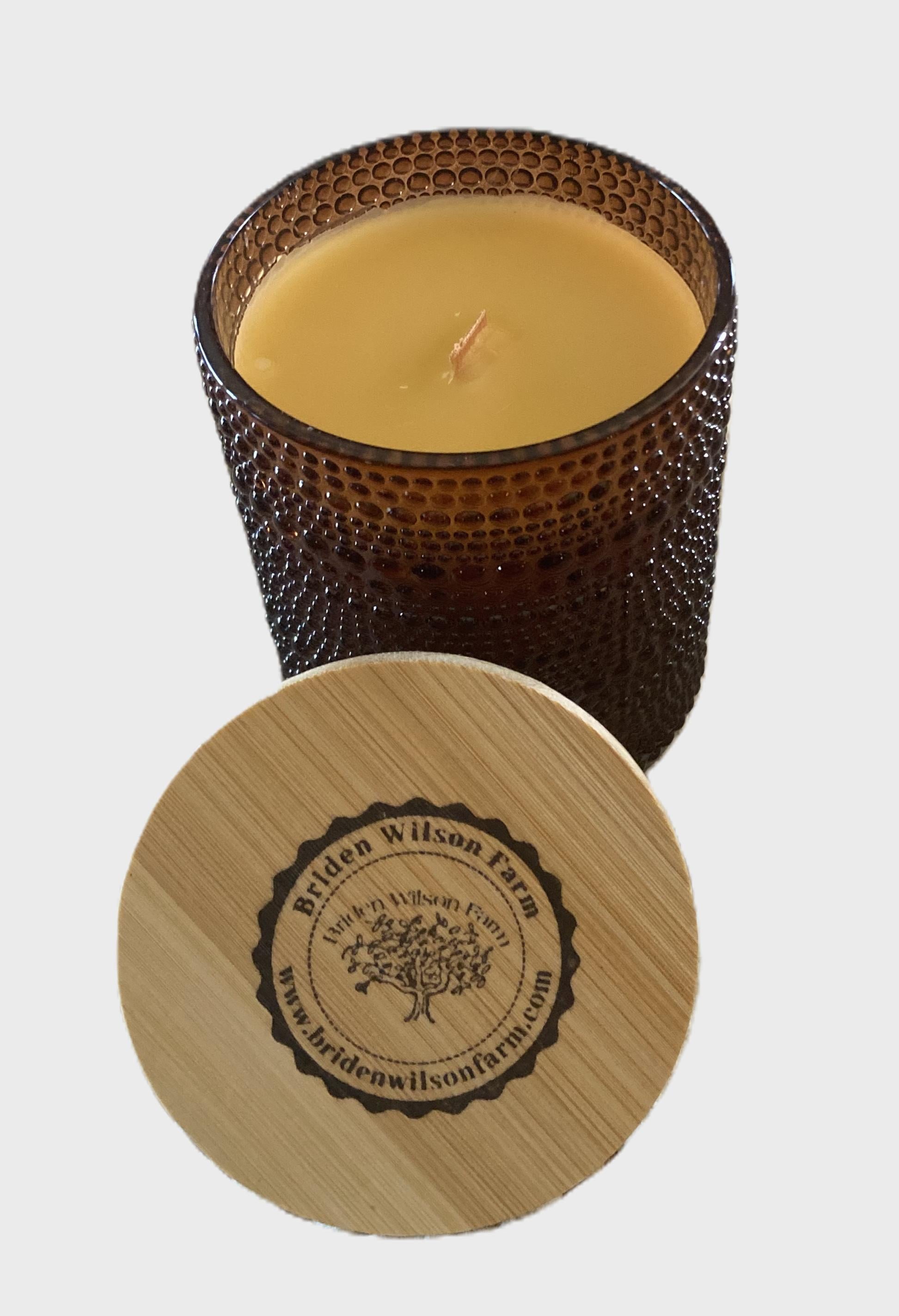 Candle in a textured brown glass container with wooden lid featuring a brand logo on a light gray background